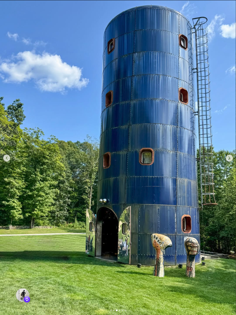 JR's blue silo Hand #5 in full sun against blue sky with sculptural figures at the base
